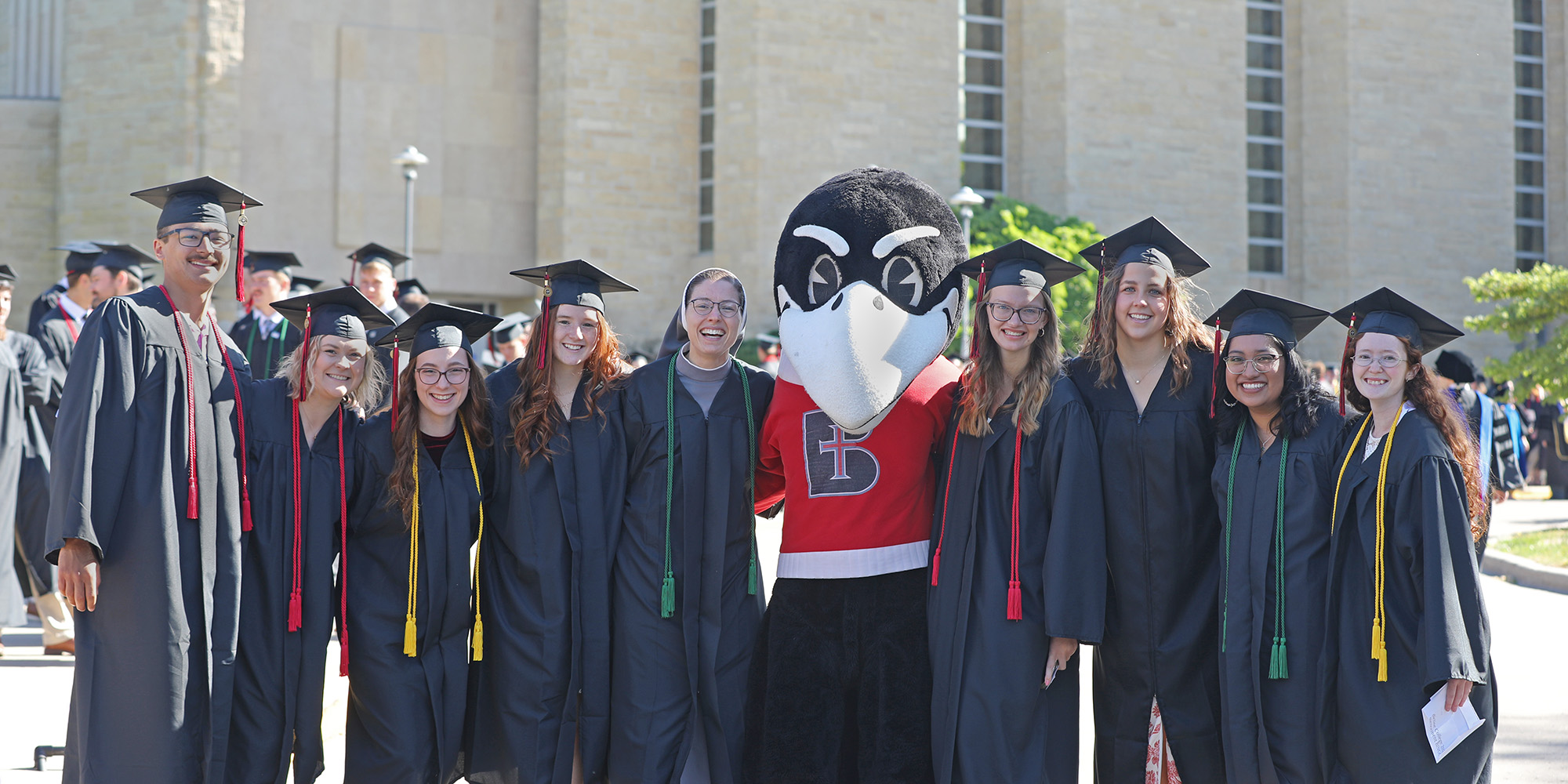 Graduates pose with Rocky the Raven before the Commencement ceremony